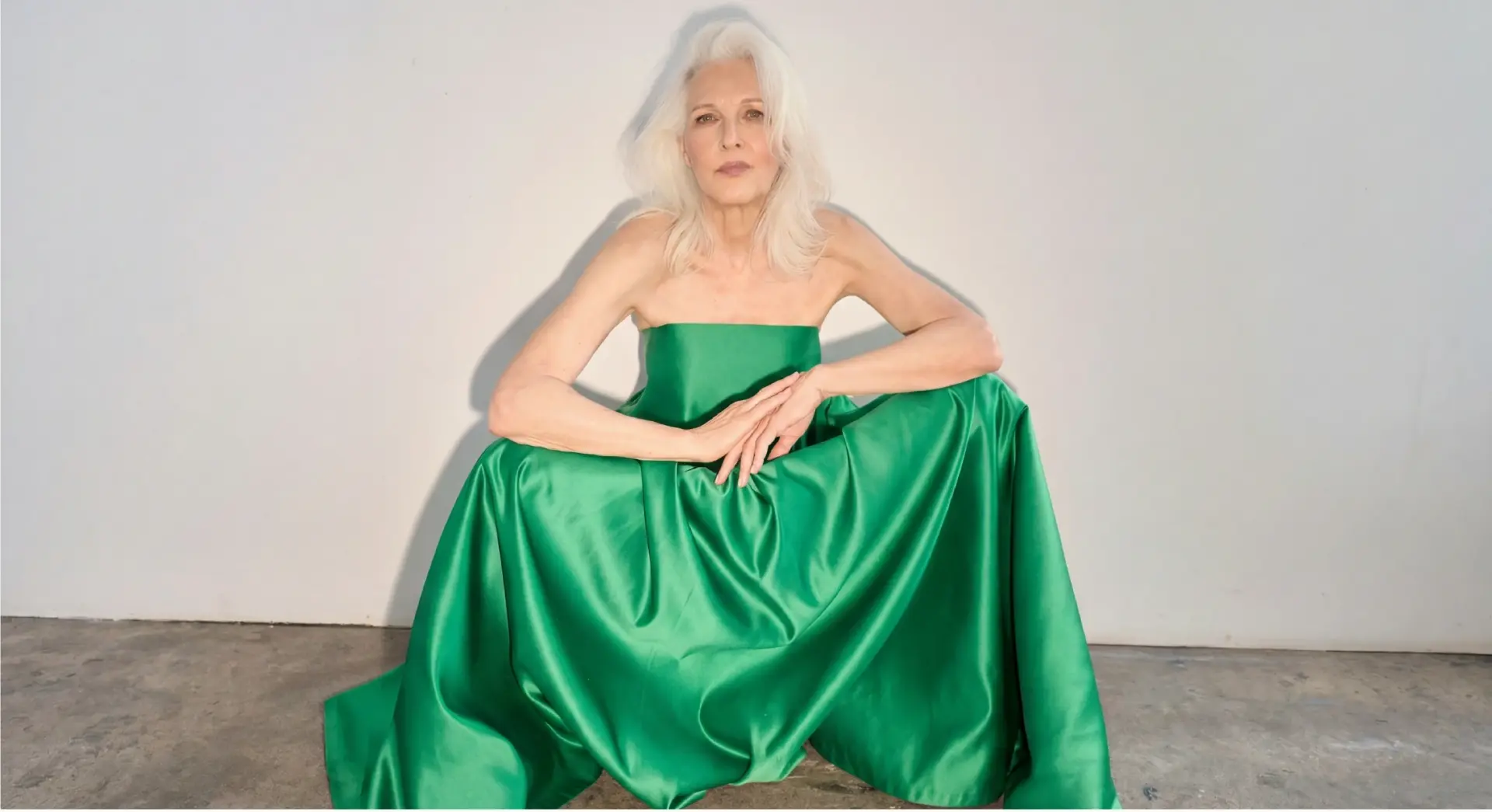 Woman in an emerald green strapless gown seated on a grey floor